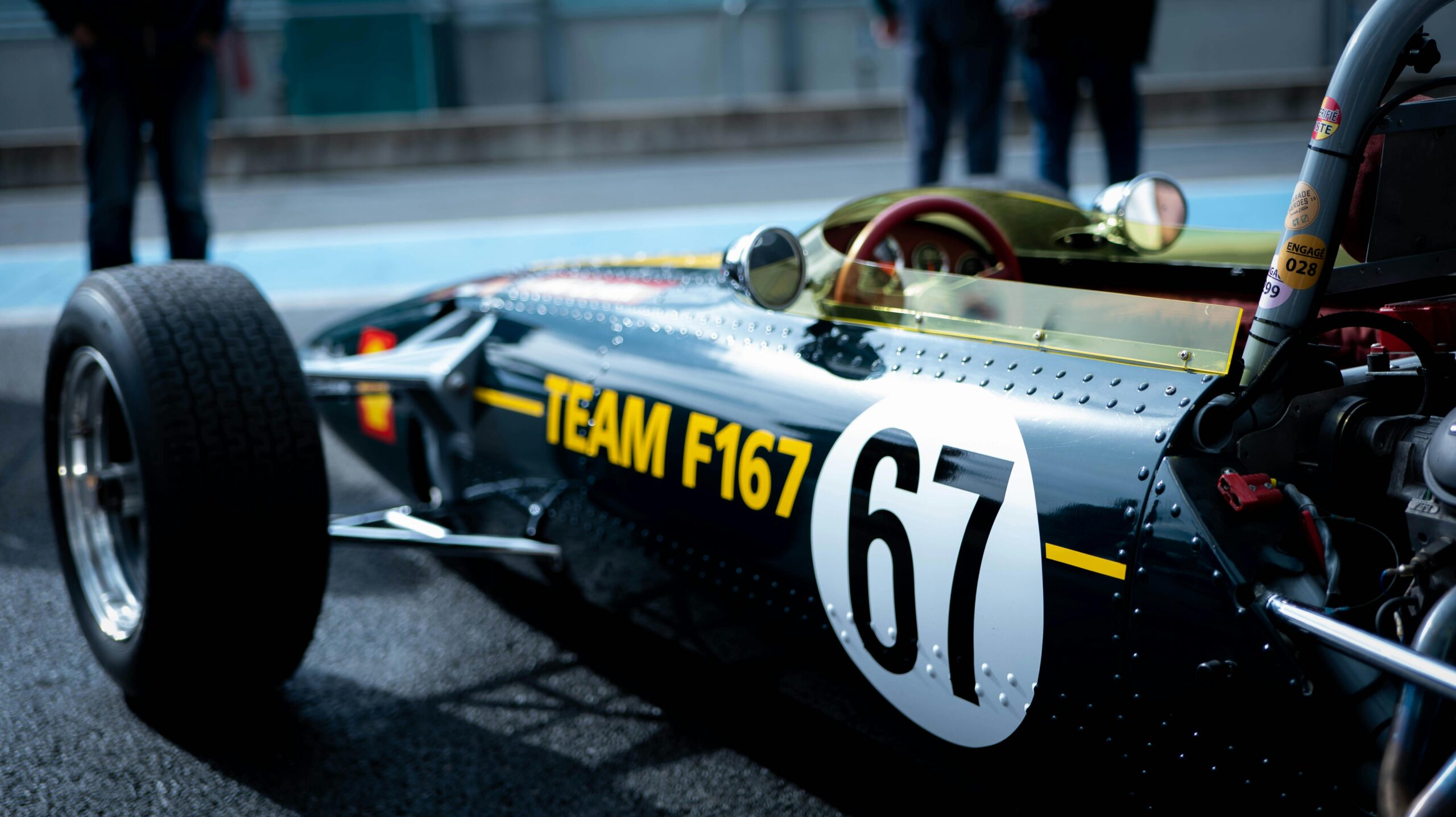A detailed view of a classic racing car with black livery and number 67 in a motorsport setting.
